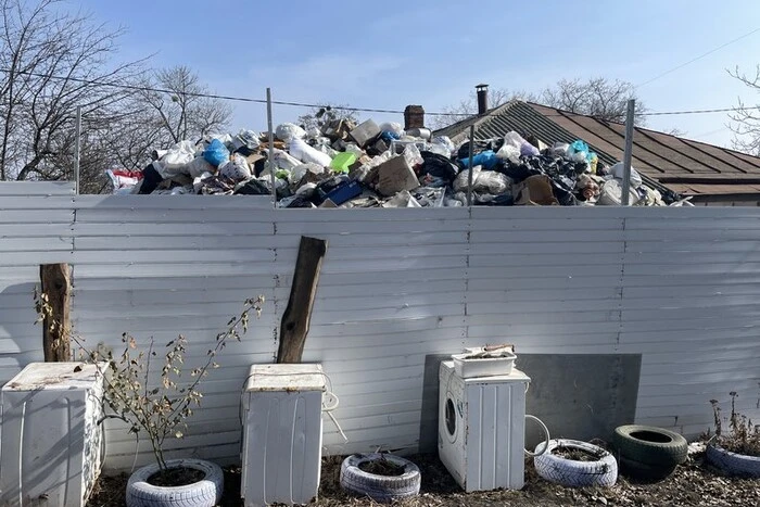 An elderly woman among garbage in the yard